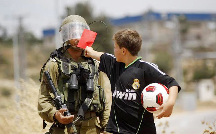 A Palestinian boy shows a red card to an Israeli soldier